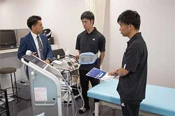 JFA 夢フィールド(海浜幕張)内のトレーナールームに設置された低周波治療器、超音波治療器、超短波治療器等と製品説明の様子